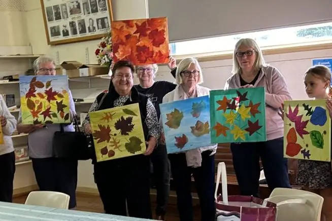 Members of the Que Club give painting lessons to some of the residents of Southern Cross Aged Care Home. Image supplied.